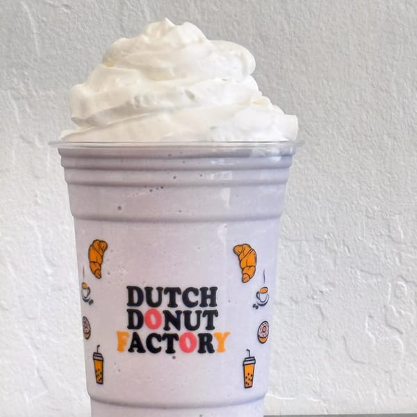 A Dutch Donut Factory branded cup filled with a light purple drink and topped with whipped cream.
