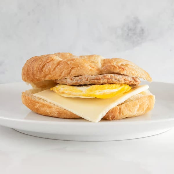 A croissant breakfast sandwich with sausage, egg, and cheese on a white plate.