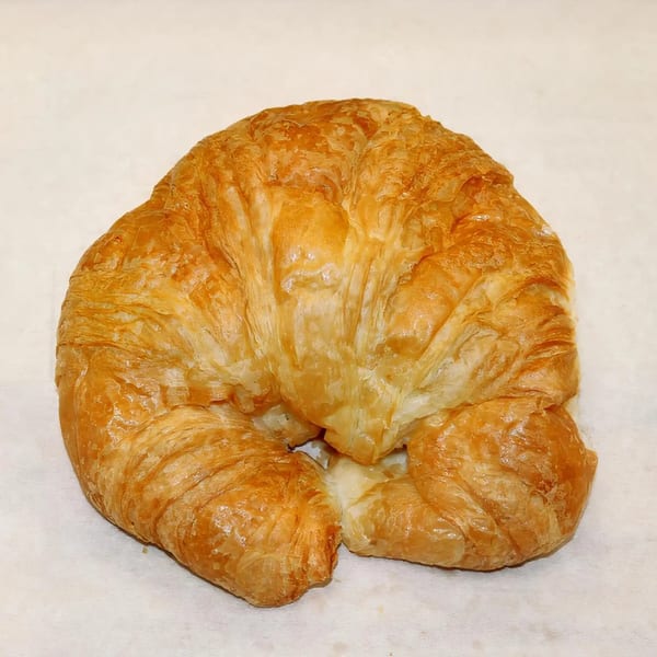 Golden-brown, flaky croissant from Dutch Donut Factory on a white surface.