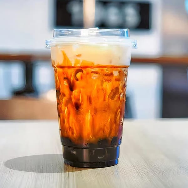 A clear plastic cup of iced coffee with a creamy top layer and dark boba pearls on a wooden table.