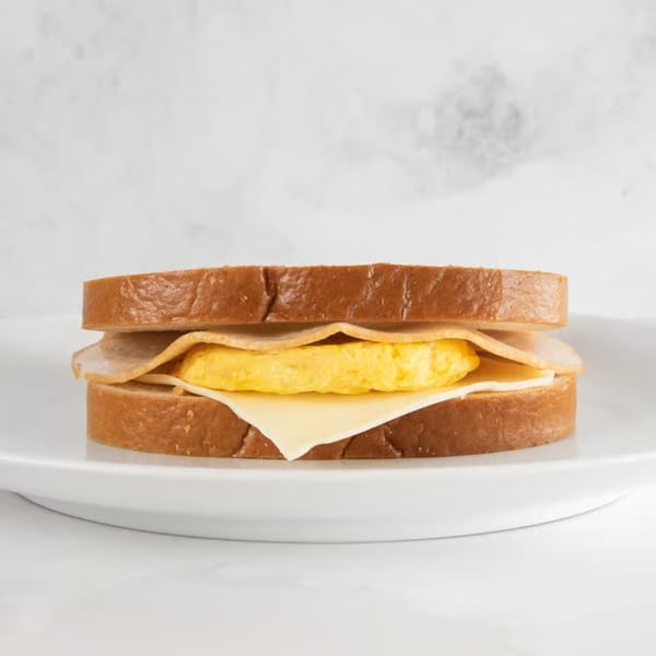 Breakfast sandwich with egg, cheese, and turkey on toasted bread, served on a white plate.