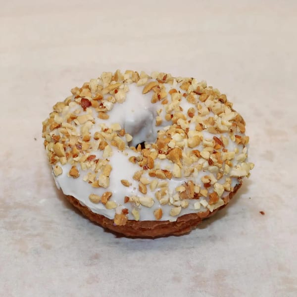 Dutch Donut Factory's donut with white icing and chopped nuts on a light background.