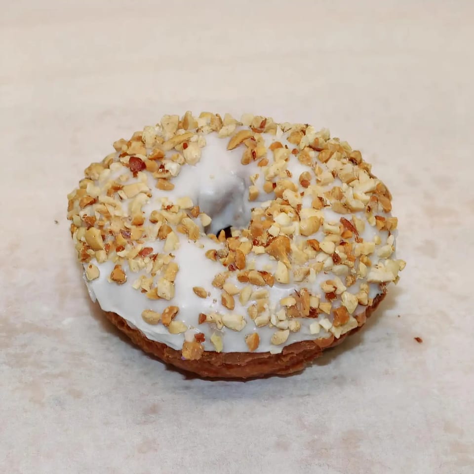 Dutch Donut Factory's donut with white icing and chopped nuts on a light background.