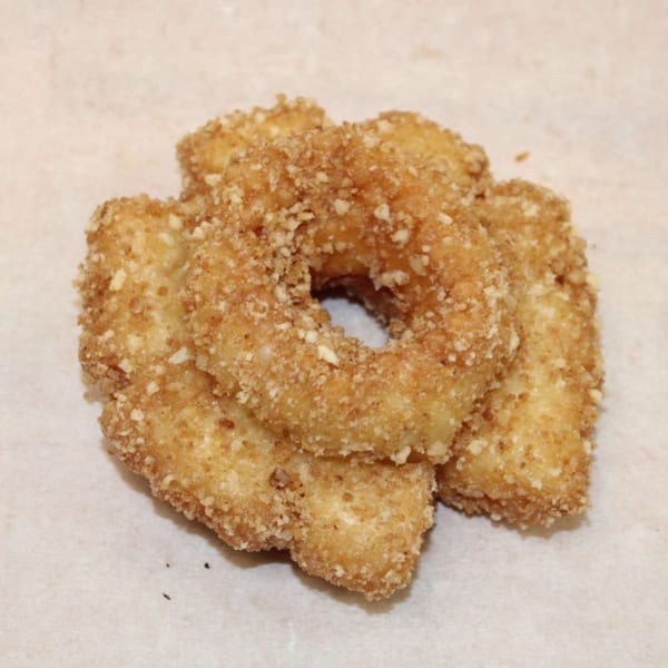 A close-up of several golden-brown, breaded onion rings piled on a light surface.