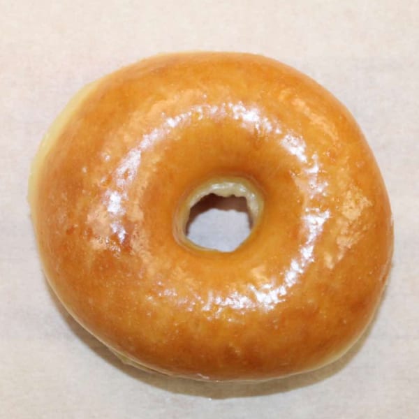 A single glazed donut with a shiny, golden-brown finish sits on a light-colored surface.